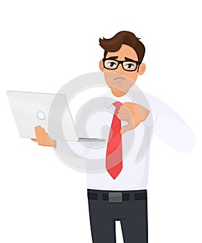 Unhappy young businessman holding laptop computer and showing thumbs down gesture. Person making dislike, bad, disagree sign.