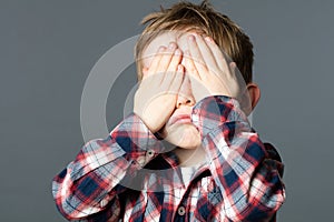 Unhappy young child covering his eyes with hands for sadness