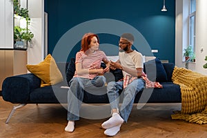 Unhappy young diverse married couple sitting on sofa talking about problems in relationship