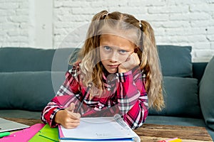 Unhappy young elementary student schoolgirl studying and doing homework at home