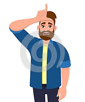 Unhappy young hipster man showing loser sign on forehead with fingers. Stressed trendy person gesturing hand over head. photo