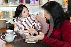 Unhappy young indian woman having conflict with boyfriend at cafe