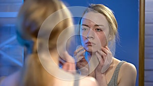 Unhappy young lady looking in mirror reflection, skin imperfection, insecurity