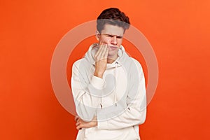 Unhappy young man in casual style sweatshirt with hood suffering from terrible toothache, gingival inflammation, oral hygiene,