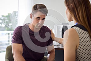 Unhappy Young Man With Depression At Appointment With Female Doctor Or GP In Office