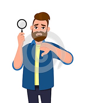 Unhappy young man holding magnifying glass and gesturing thumbs down sign. No deal, bad, disagree, search, find, discovery.