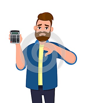 Unhappy young man showing or holding a digital calculator device in hand and gesturing, making thumbs down sign. Bad, dislike.