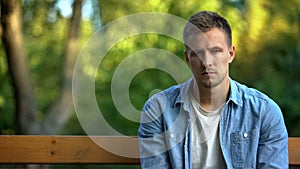 Unhappy young man sitting alone bench thinking problem, trouble depression