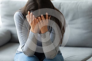 Unhappy young woman covering face with hands, crying alone