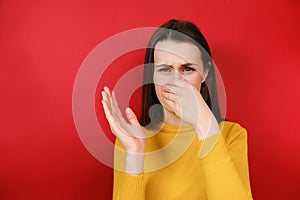 Unhappy young woman covers nose with hand, smells something awful, pinches nose, frowns in displeasure, dressed in yellow sweater