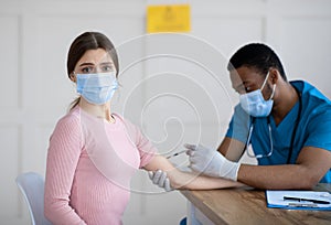 Unhappy young woman in face mask feeling afraid of pain during covid-19 vaccine shot at medical office