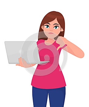Unhappy young woman holding laptop computer and thumbs down gesture. Trendy girl using gadget and showing bad or dislike sign.