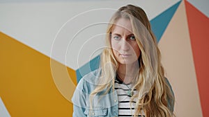 Unhappy young woman is looking at camera with sad face standing alone indoors