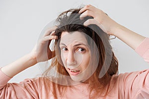 Unhappy young woman scratches head with hands caused by dandruff