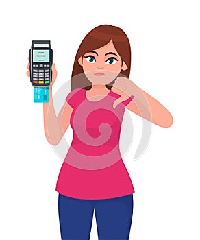 Unhappy young woman showing/holding pos payment terminal or credit/debit cards swiping machine, gesturing thumbs down sign.