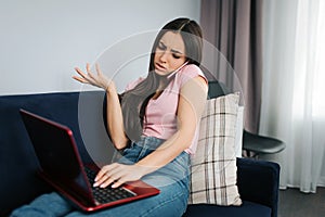 Unhappy young woman sit on sofa and talk on phone. She complain. Modle type on keyboard. She work at home. photo