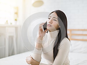 Unhappy young woman talking on mobile phone at home