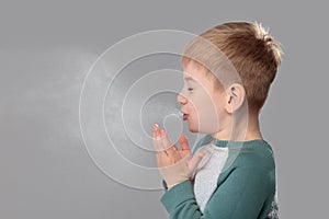 Unhealthy boy snezzing very hard over grey background