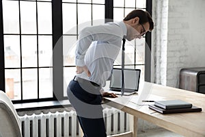 Unhealthy businessman touching lower back, suffering from backache in office