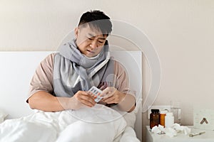Unhealthy chinese man sitting in bed, taking pills