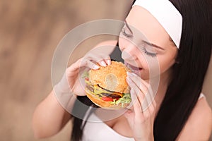 Unhealthy eating. Junk food concept. Portrait of fashionable young woman holding burger and posing over wood background. Close up.