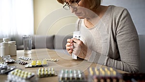 Unhealthy elderly female depressed about taking too much medicine, holding pills