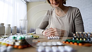 Unhealthy elderly lady suffering pain looking at pills, painkillers hypochondria