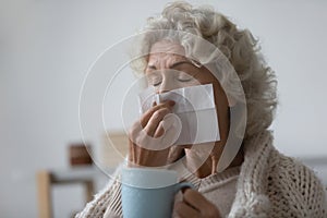 Unhealthy elderly woman wiping runny nose with paper tissue.