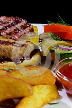 Unhealthy food.Burger with fried bacon, french fries, vegetables and ketchup on a white plate.Close-up