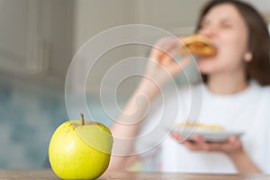 Unhealthy food choices. Wrong nutrition and overeating. Woman eats cheeseburger and fries against apple