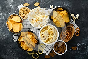 Unhealthy food. Snacks. All classic potato snacks with peanuts, popcorn and onion rings and salted pretzels in bowl plates on