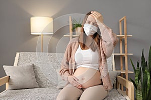 Unhealthy ill pregnant female wearing medical mask having virus suffering flu grippe symptoms touching her belly keeps hand in