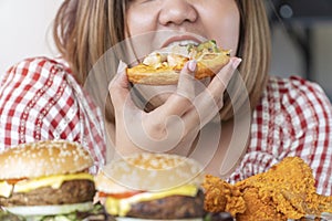 Unhealthy junk food concept. Hands of oversize fat woman eating pizza with hamburger and chicken fried on table. Close up