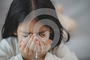 An unhealthy kid blowing their nose into a tissue, a Child suffering from running nose or sneezing, A girl catching a cold when