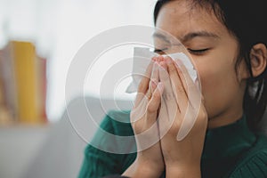 An unhealthy kid blowing their nose into a tissue, a Child suffering from running nose or sneezing, A girl catching a cold when
