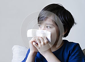 Unhealthy kid with dry skin blowing nose into tissue, Child suffering from running nose or sneezing , A boy catches a cold when