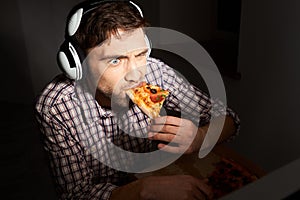 Unhealthy lifestyle. Junk food, fast food.Sloe up portrait of young bearded male gamer with short hair in casual shirt