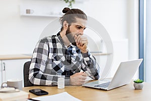 Unhealthy male in shirt coughing into fist while sitting at desk with computer.