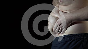 Unhealthy man checking his belly in front of dark background.