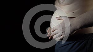 Unhealthy man checking his belly in front of dark background.