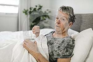 Unhealthy mature woman lying in bed, taking medicine from cold or insomnia