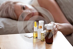 Unhealthy mature woman lying in bed, taking pills close up