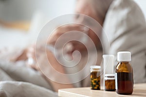 Unhealthy mature woman suffering from cold, meds on bedside table