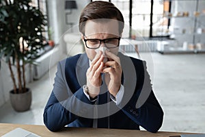 Unhealthy millennial businessman suffering from runny nose.