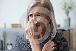 Unhealthy older woman covered in plaid, using paper tissue.