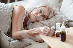 Unhealthy older woman taking pills from bedside table close up