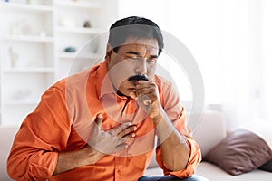 Unhealthy sick indian middle aged man coughing, home interior