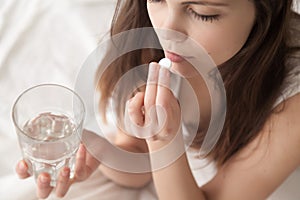 Unhealthy sick young woman taking sleeping pill sitting in bed