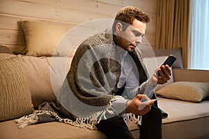 Unhealthy tired man sitting on sofa and holding mobile phone