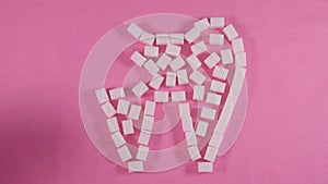 An unhealthy tooth with caries is lined with refined sugar cubes on a pink background.